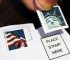 Hand holds Statue of Liberty stamp over envelope. Explore options to reuse stamps for mailing.