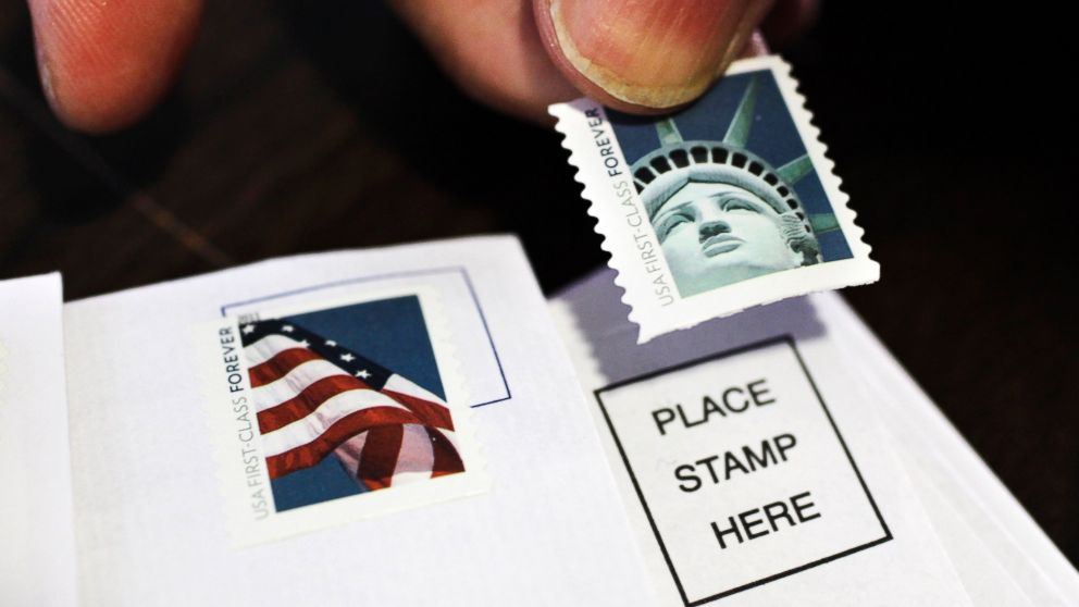 Hand holds Statue of Liberty stamp over envelope. Explore options to reuse stamps for mailing.